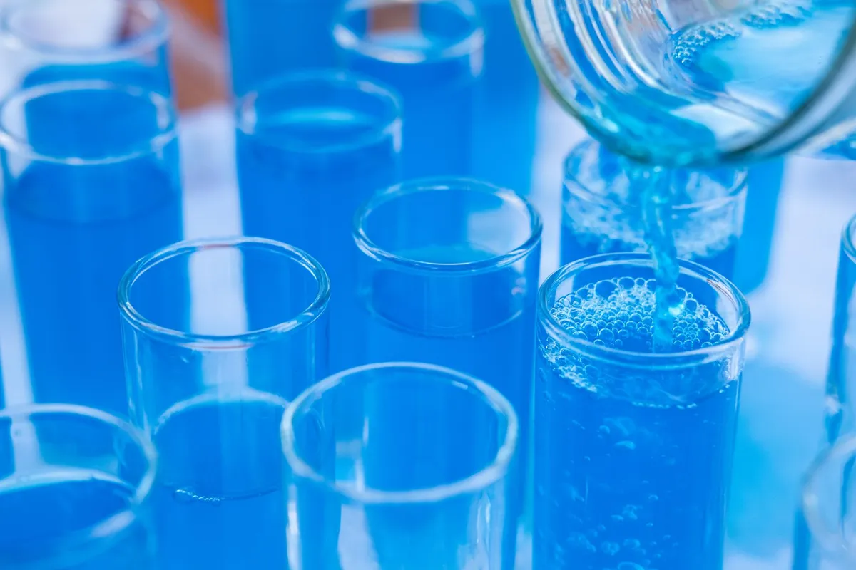 A glass of clear drinking water on a light surface beside a laboratory filtration setup in natural light